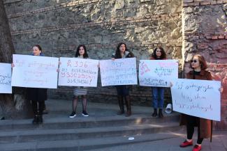 The photo depicts five women (Sopo is standing in the middle) standing on top of stairs in front of a stone wall, holding placards with Georgian slogans written on them.